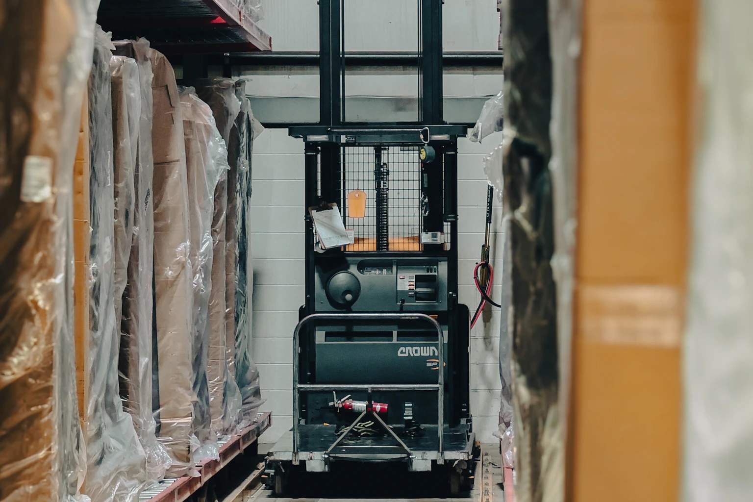 Forklift in a warehouse aisle with racked and wrapped inventory