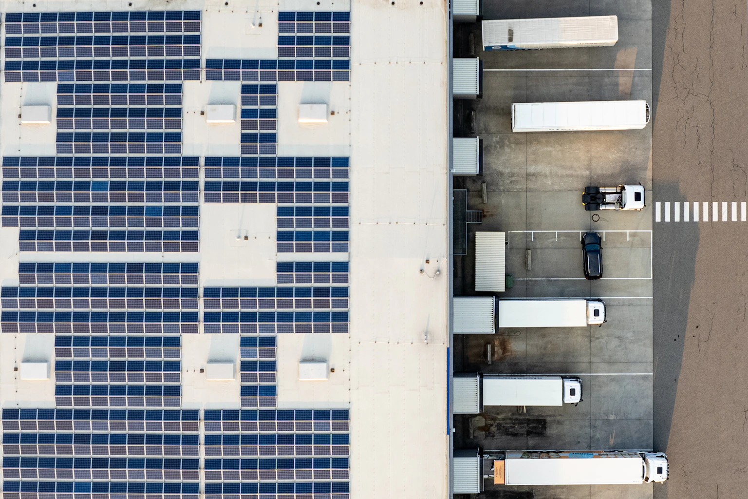 Aerial photograph of solar panels on an industrial warehouse roof beside loading bays