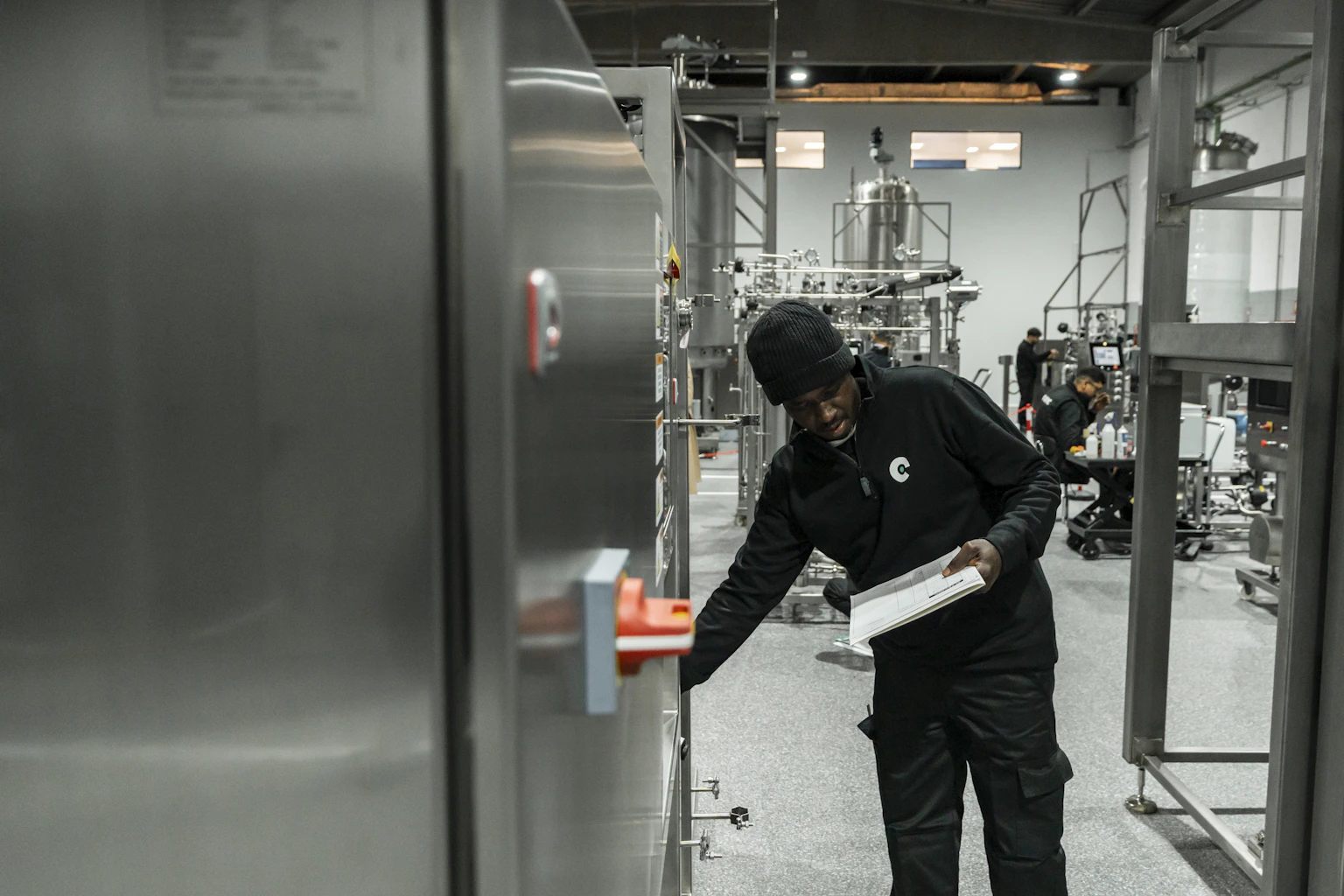 Technician inspecting manufacturing equipment while recording checks on a clipboard